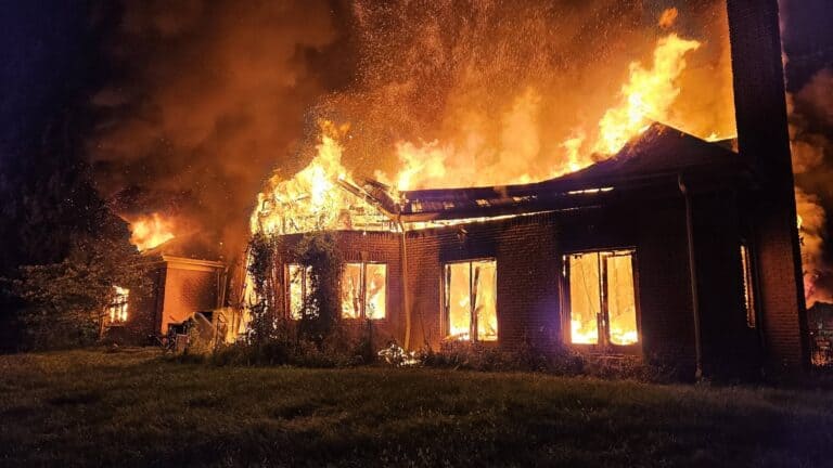 A brick house engulfed in flames at night.