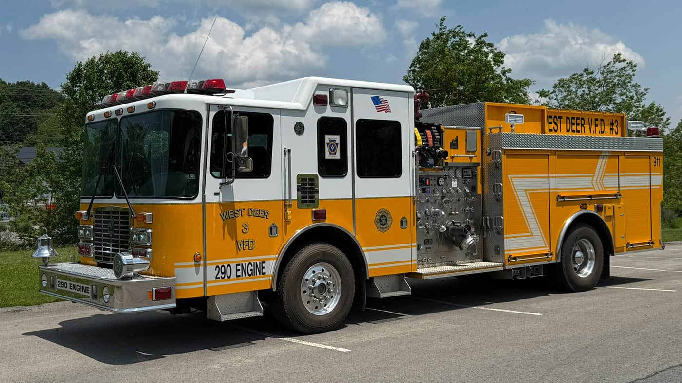 A yellow and white fire truck labeled “West Deer VFD 290 Engine” is parked on a paved road with trees and a partly cloudy sky in the background.