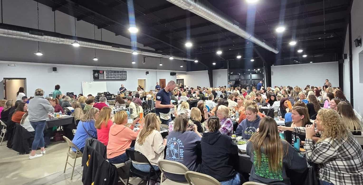 A large group of people seated at tables in a spacious room, participating in a group event or workshop.