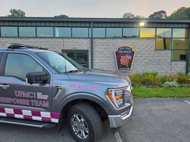 A gray UPMC Response Team Medic 269 truck parked in front of a building with a West Deer Fire Rescue Station 290 sign on the wall.