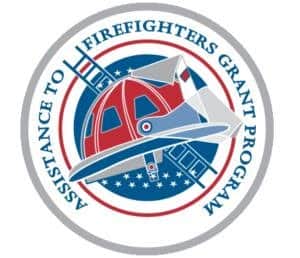 Circular logo for the Assistance to Firefighters Grant Program featuring a red and white fire helmet and a ladder over a blue, star-spangled background.